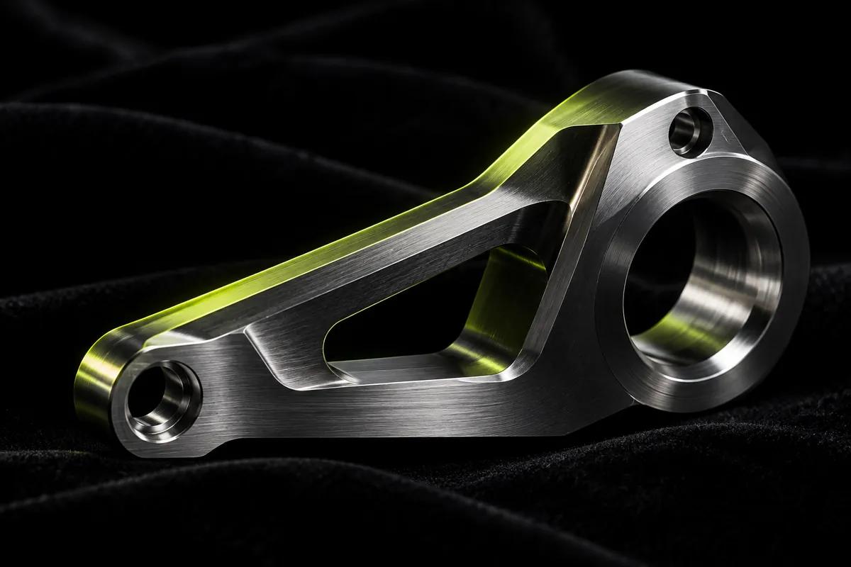 A single machined metal part on black velvet, lime light along one machined face