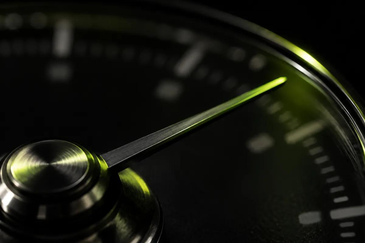A precision gauge needle in close-up, its scale markings blurred, with a lime reflection