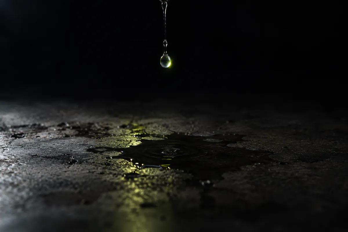 A drop of water falling onto a dark concrete floor, catching a lime highlight